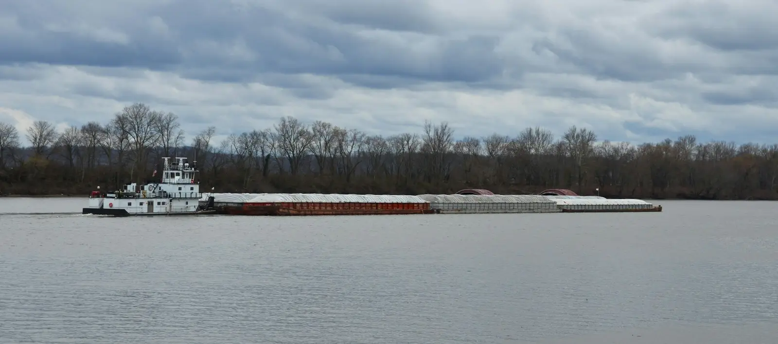 A tug pushing a line of loaded barges along a wide river