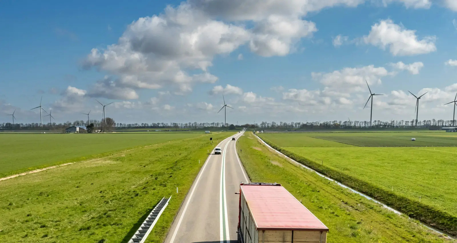 A truck on a straight road across open farmland towards the horizon