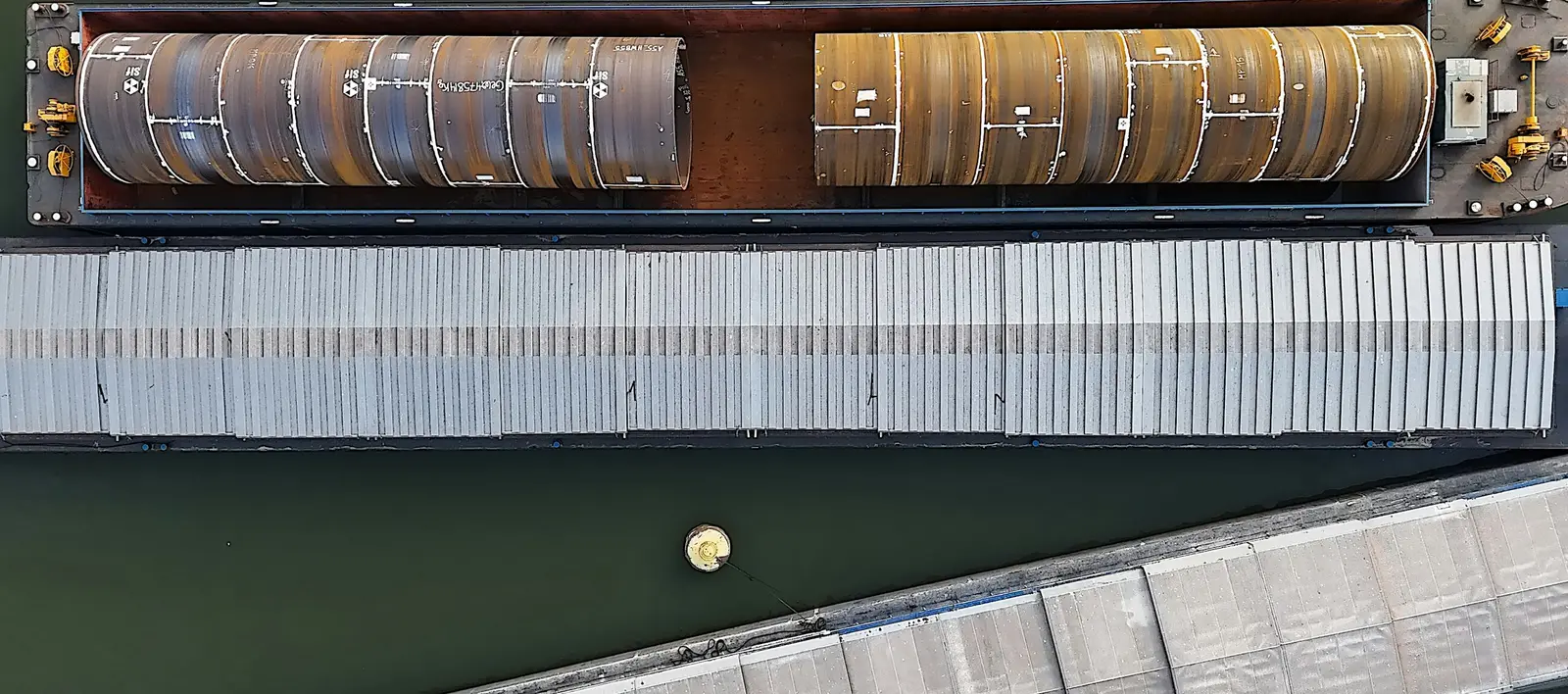 Barges carrying large steel pipes, seen from above