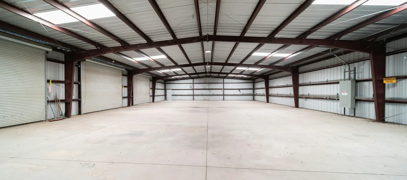 The empty interior of a steel-framed warehouse with roller doors